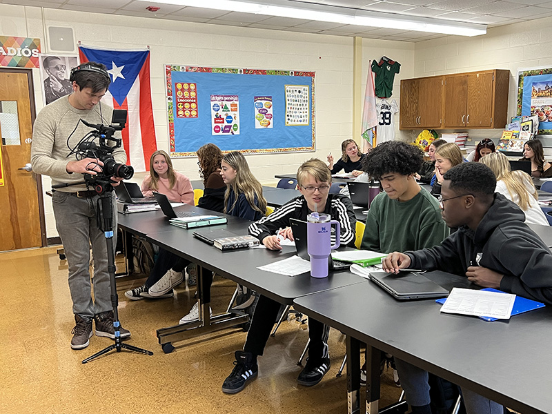 A man videos a group of high school kids who are working on a Spanish project.