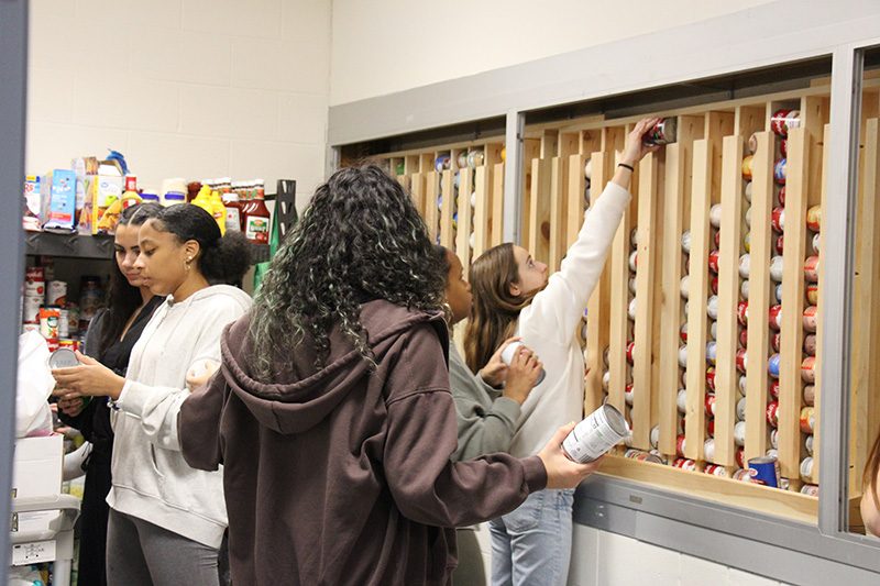 High school girls reach up high to stack cans in a rack on the wall.