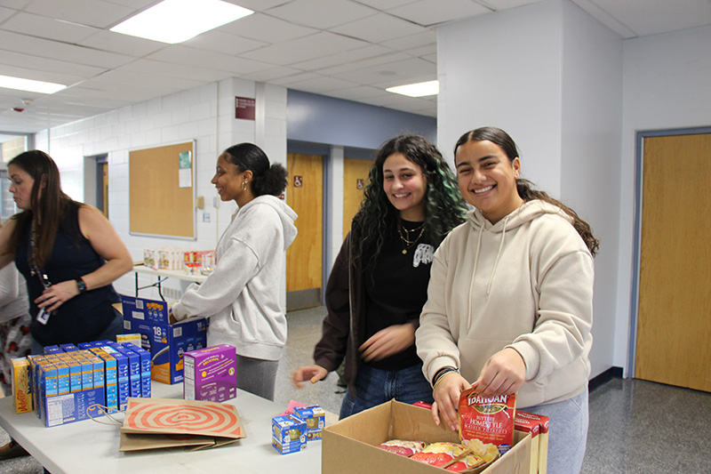 High school girls sort through food and put in boxes and bags. Two of the girls are smiling at the camera.