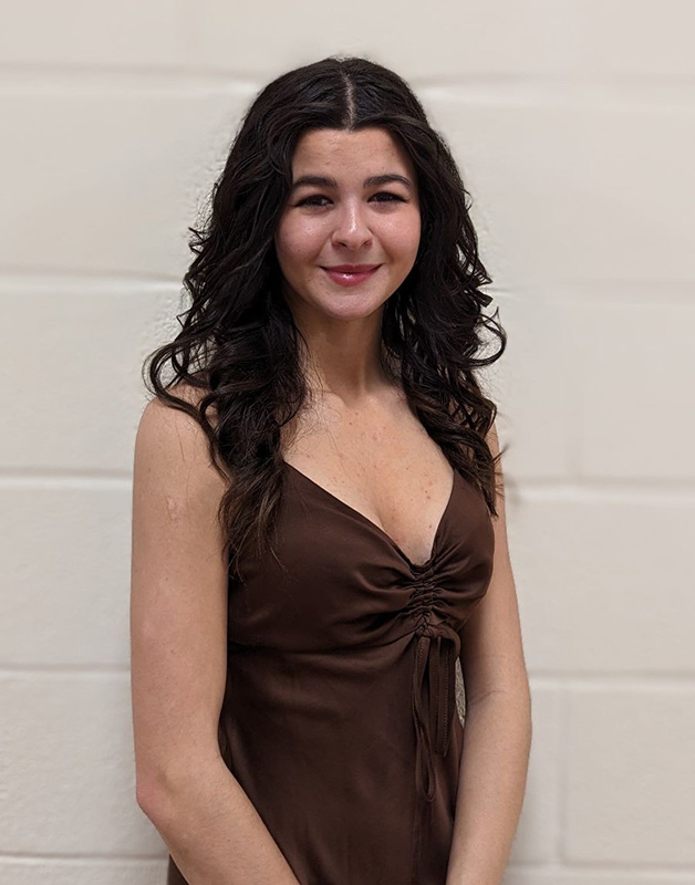 A young women with long dark hair,wearing a dark colored dress. She is smiling.