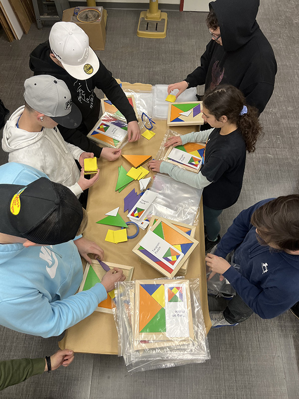 A photo from overhead. A group of five high school students put small puzzles into plastic bags.