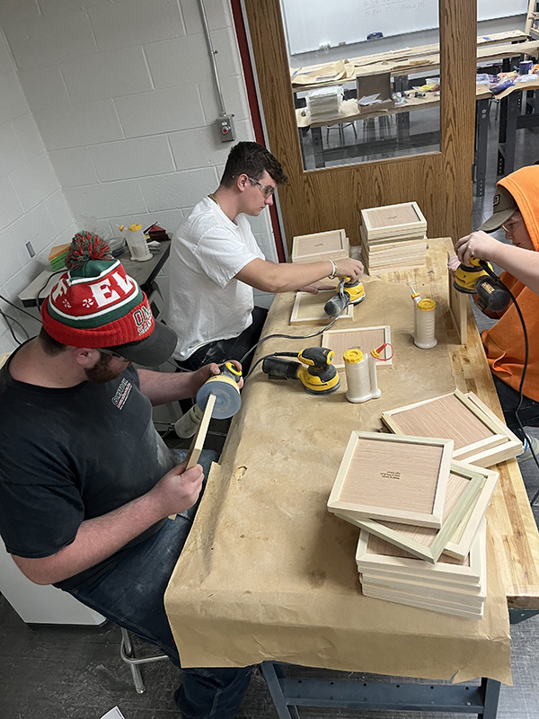 A group of three high school students make wood puzzles.