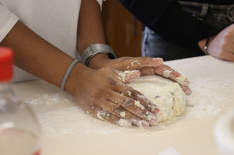 Dough sitting on table with two hands around it, shapin git.