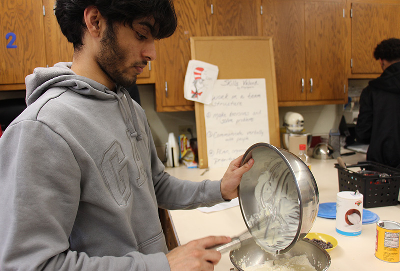 A high school boy uses a whisk to mix ingredients for scones.