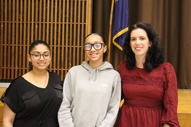 Two high school girls smile with a woman standing on the right.