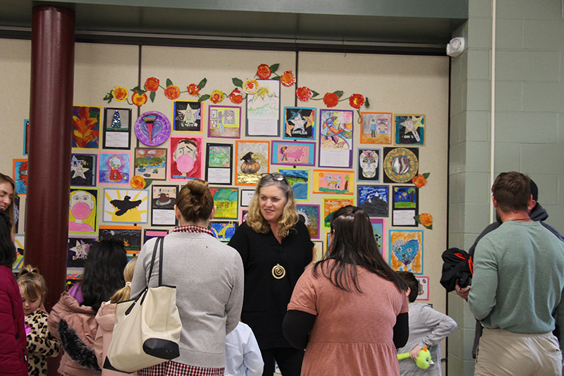 A wall filled with artwork. There are people looking at the wall.