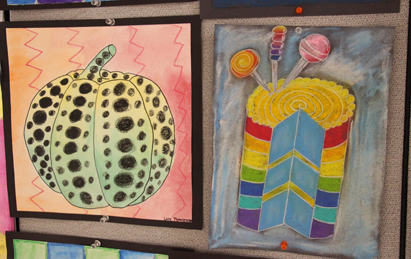 Artwork made by elementary students. The one on the left is a pumpkin and the one on the right is a multi-color cake with a slice cut out.