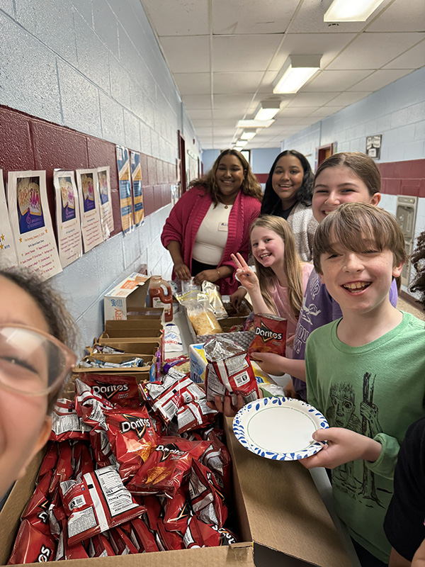 A long line of fifth-graders smile as they get their food from a table in front of them.