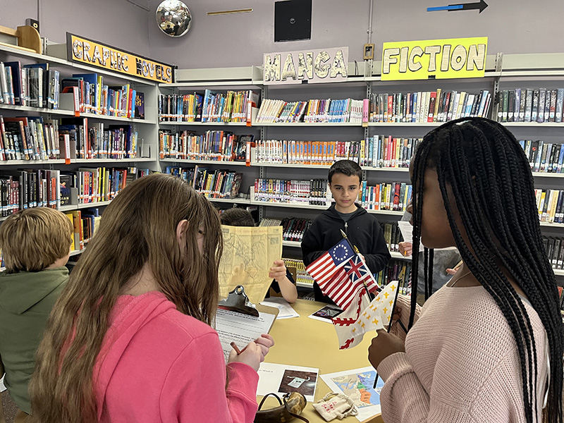 Three middle school students stand around Revolutionary War artifacts.