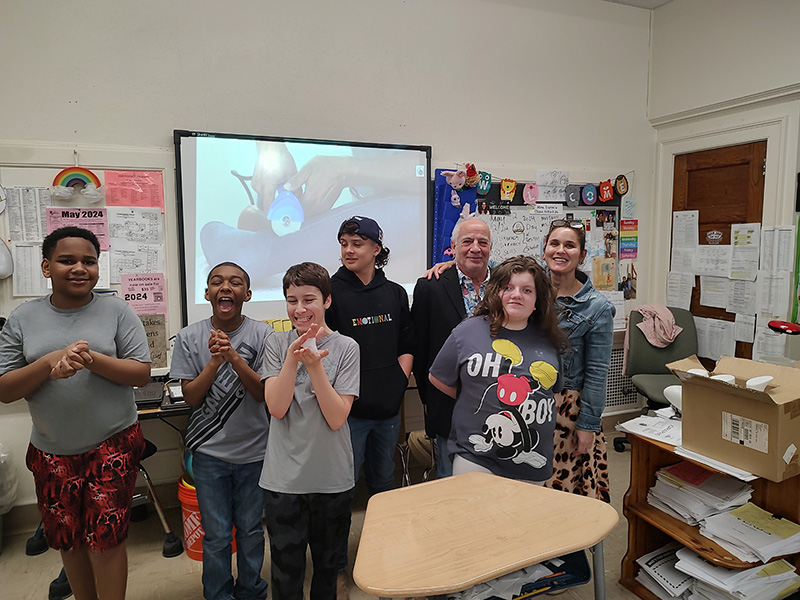 A group of five middle school students stand together with an older man. They are smiling.