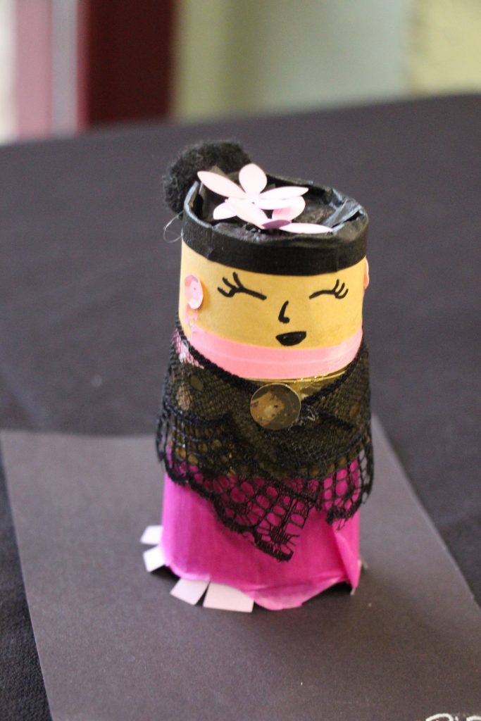 A piece of three-dimensional artwork. It is a girl with dark hair and a flower on top.