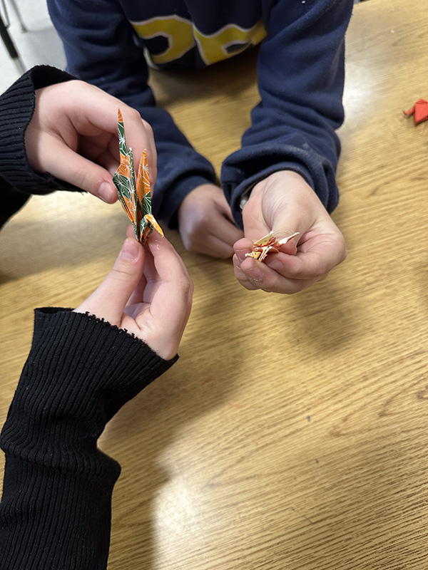 Two sets of kids hands making tiny paper cranes.