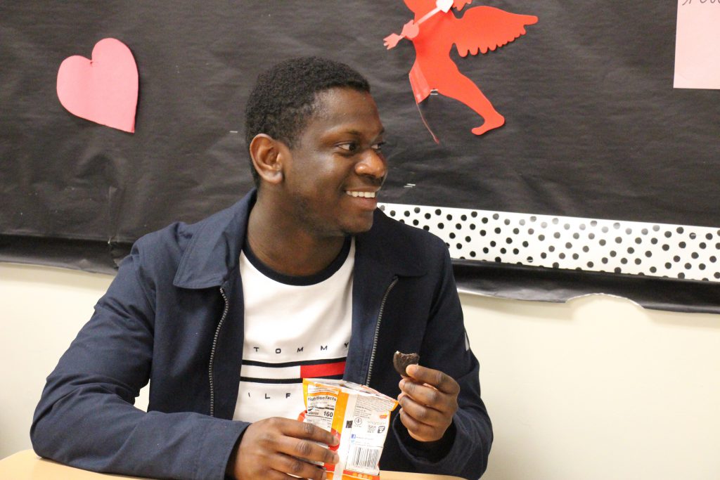 A high school student, a young man, smiles as he eats some snacks.