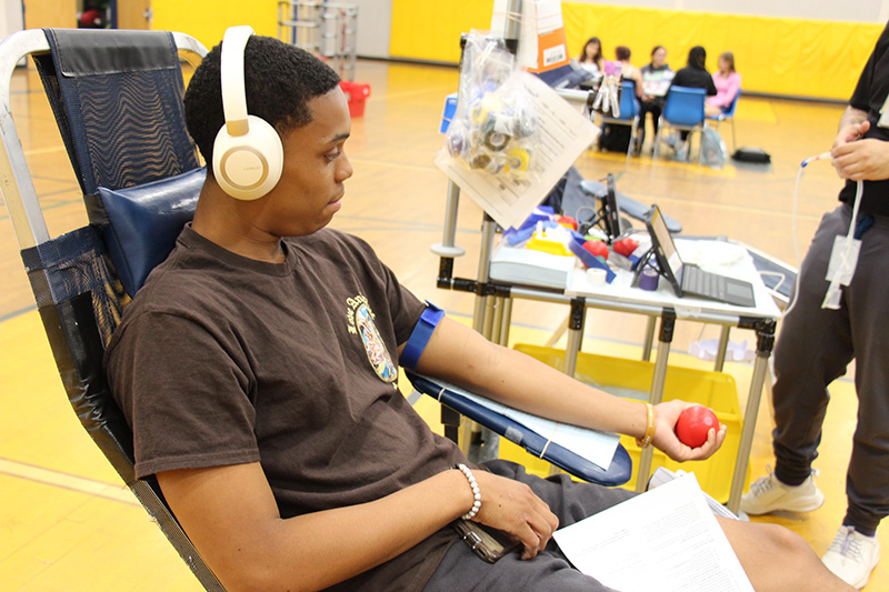 A high school students with headphones on squeezes a red ball, preparing to donate blood.