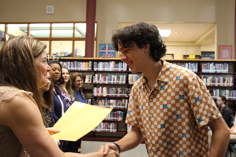 A high school boy shakes hands with a woman and gets an envelope from her.