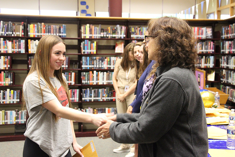 A high school girl shakes hands with a woman. They are smiling.