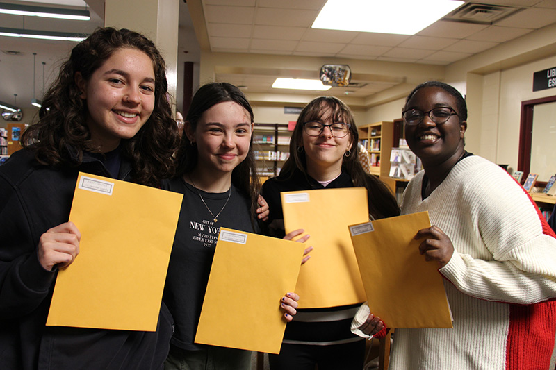 Four high school girls smile and hold up manilla envelopes they received.