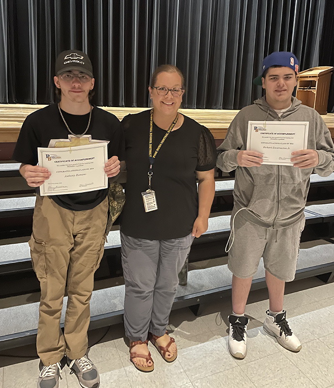 A woman stands in the center of two senior high school boys. The boys are holding certificates.