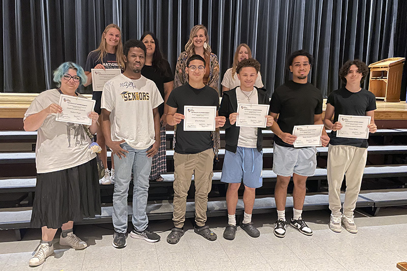 Seven high school seniors stand with three women. The students are holding certificates.