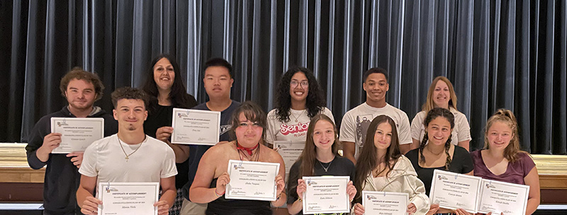 A group of 10 high school seniors each holding a certificate and smiling. Two women are standing with them.