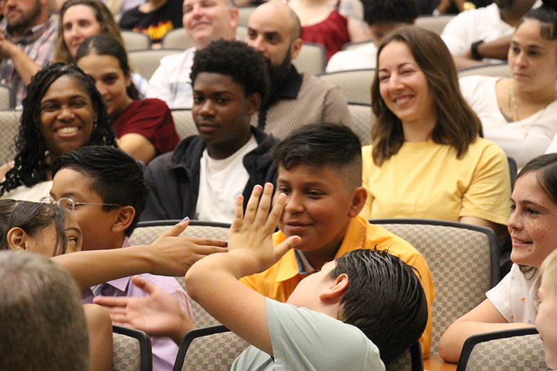 Fifth-grade students sitting. Two boys high five another boy.