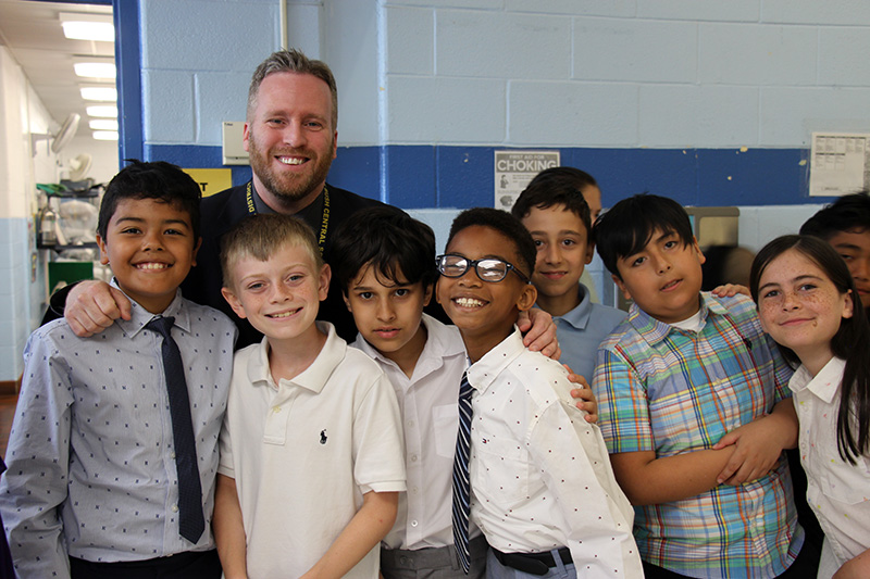 A man stands among a group of seven fifth-grade boys. All are smiling.