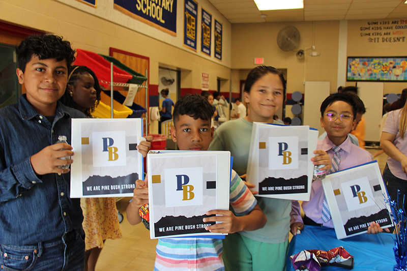 Four fifth-grade students smile and hold up binders they received with blue and gold PB on them.