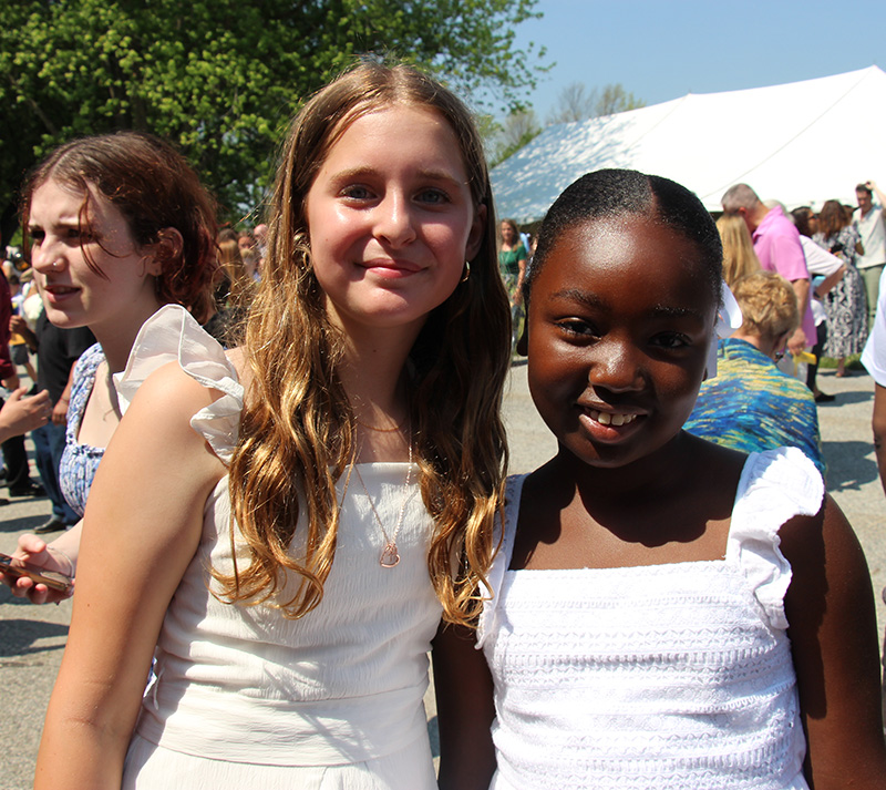 Two girls, both in white dresses, smile.