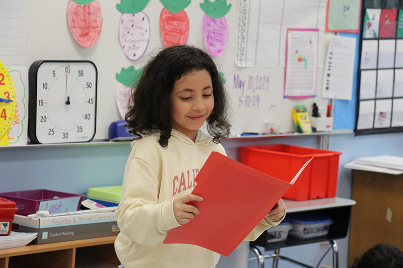 A girl with shoulder length dark hair smiles a she reads from a book