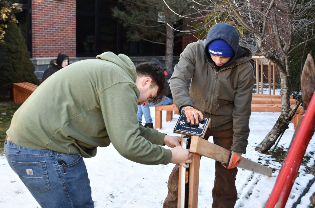 Two high school boys work on building a project with wood.