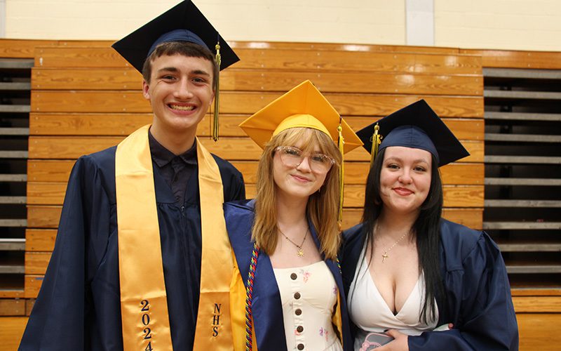 Three young people stand together. They are wearing blue and gold caps and gowns.