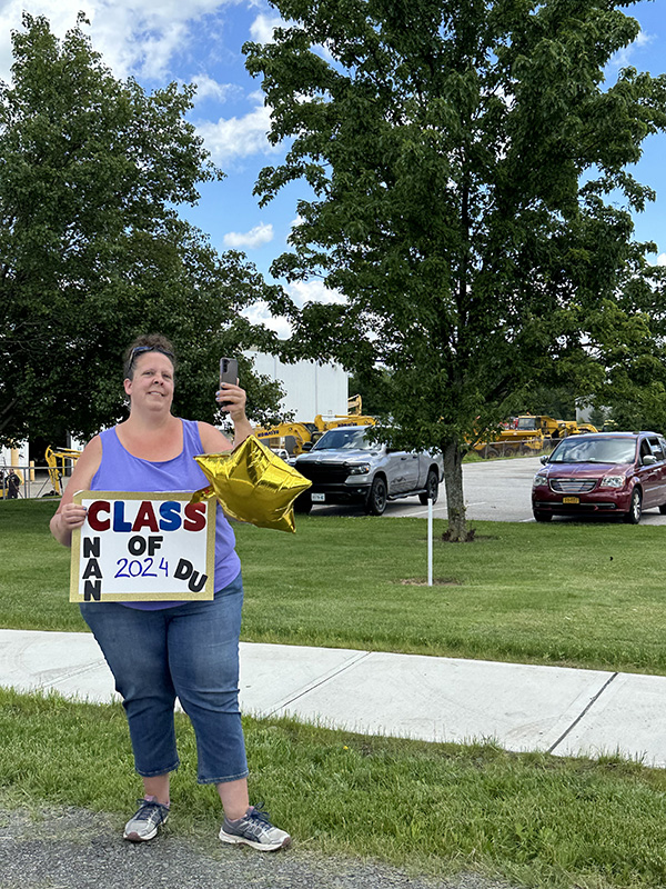 A woman with her hair pulled back holds up a sign that says Congratulations Class of 2024