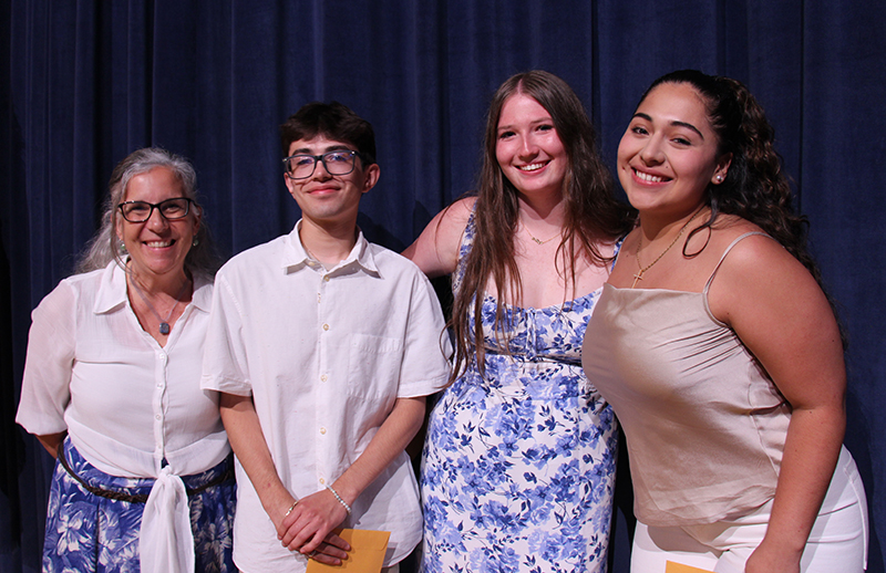 A group of three high school students and a woman on the left stand together smiling. 