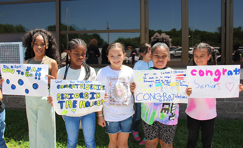 Elementary students hold congratulatory signs for high school seniors.