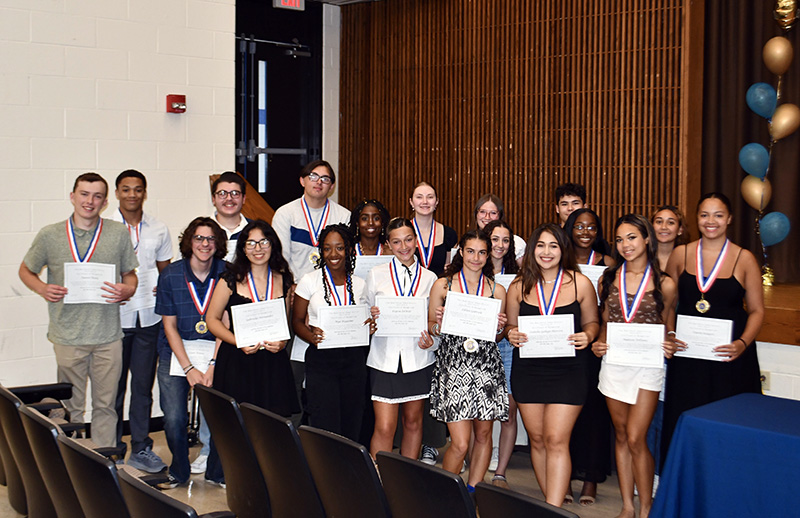 A group of 19 high school students stand in two rows, each holding a certificate.