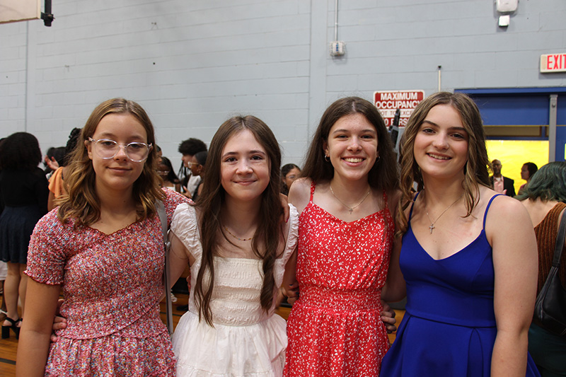 A group of four eighth-grade girls standing together smiling, arm-in-arm.