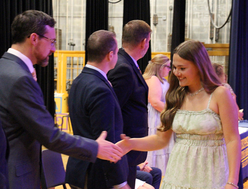 A girl with long light hair wearing a summer dress shakes the hand of a man in a suit.