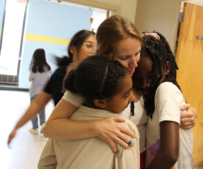 Two fifth-grade girls hug a teacher.