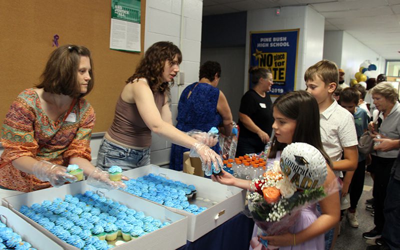 A line of fifth-grade students wait for their blue frosted cupcakes that are being handed out by adults.