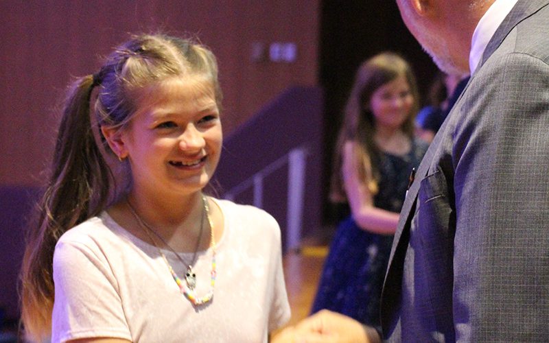 A fifth-grade girl smiles as she shakes a man's hand.