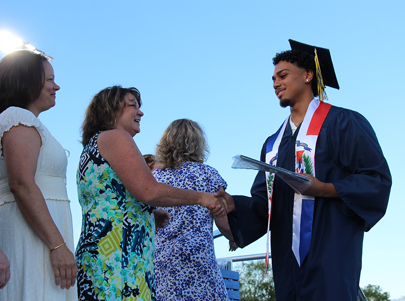 A high school graduate shakes the hand of a woman as he receives his diploma.