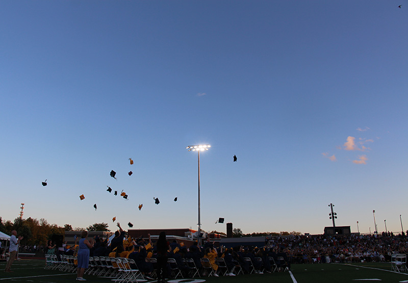 A dark blue sky with many graduation caps thrown up into the air.