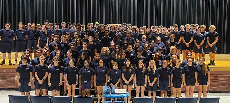 A group of more than 100 high school students in an auditorium. The students are all wearing navy blue shirts.