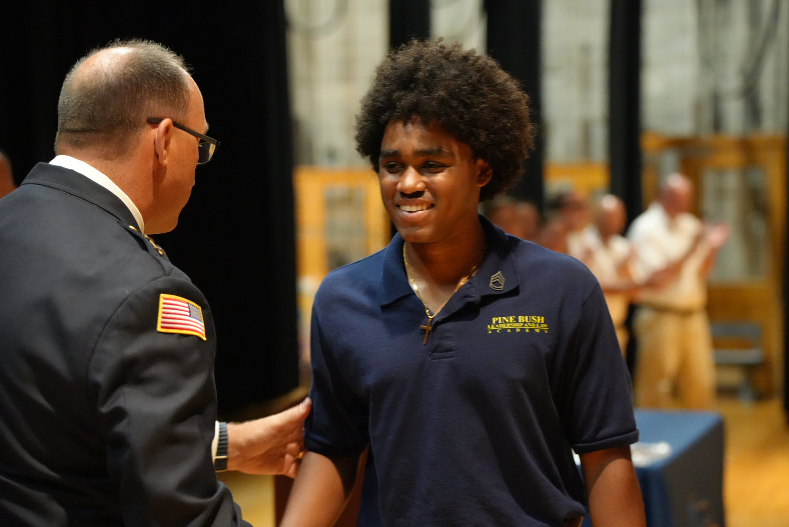 A high school boy smiles and shakes hands with a police officer.