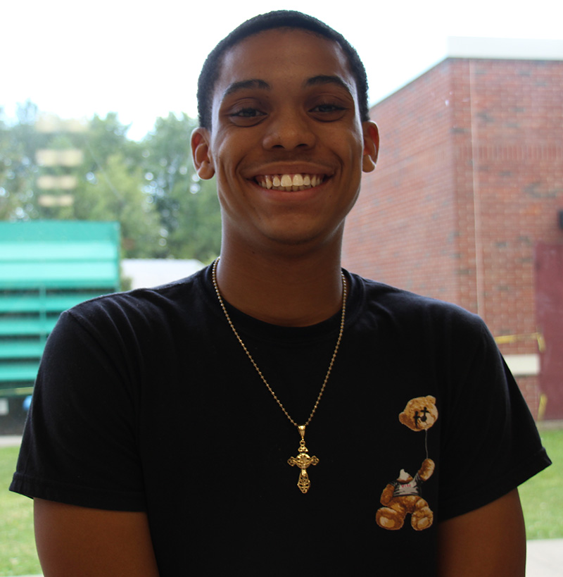 A high school young man smiles. He has short dark hair and is wearing a dark tshirt.