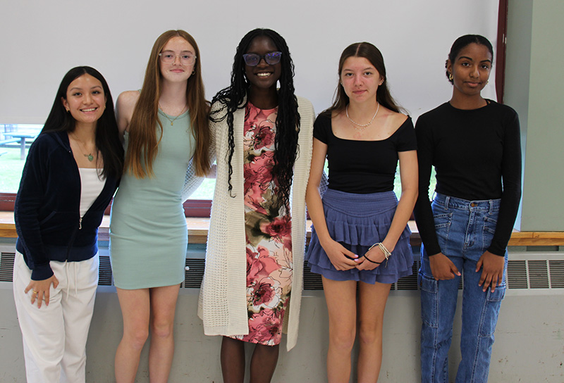 Five high school girls stand together arm in arm. they are smiling.