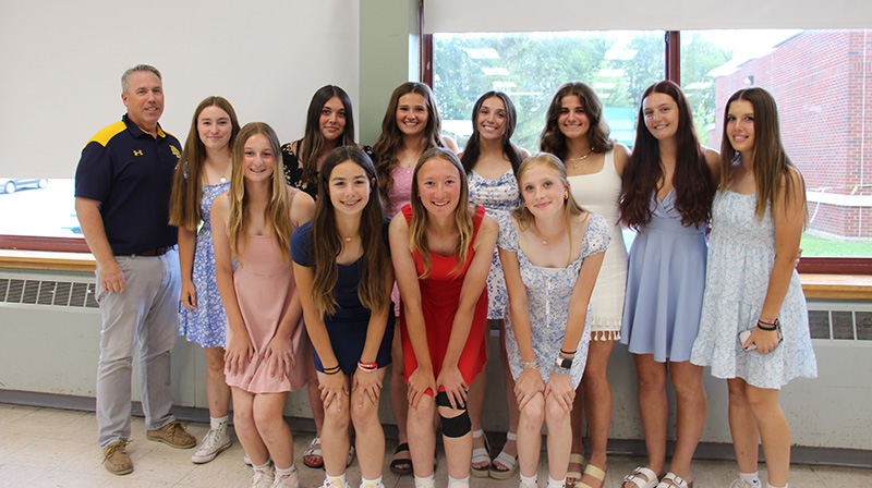 A man stands on the left. In two rows are 11 high school girls, all smiling.