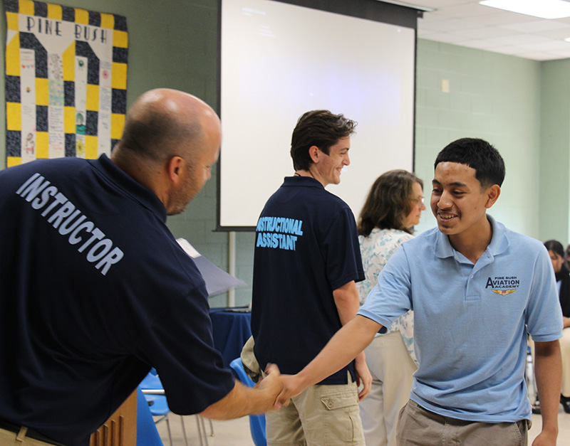 A high school boy shakes hands with a man.