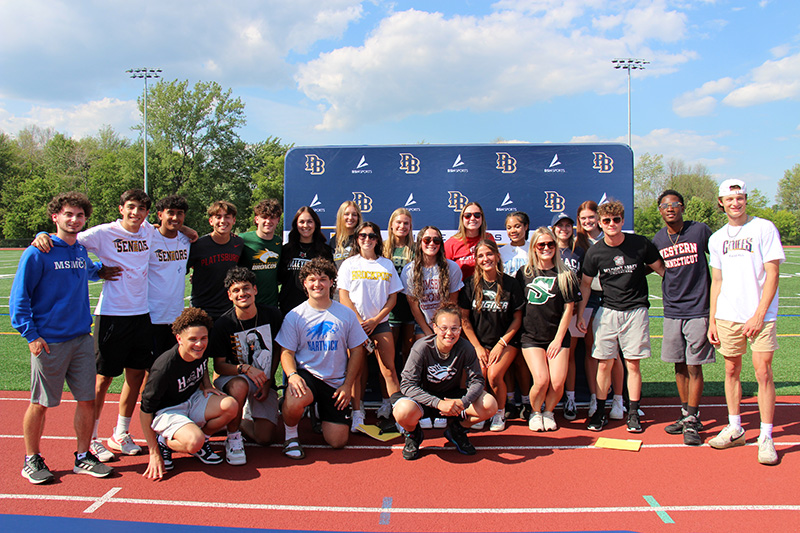 A group of 25 high school seniors stand and kneel in a group on a sunny day. They are all smiling.