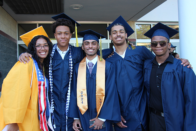 A group of five high school seniors, all wearing gold or blue cap and gown. They are smiling.